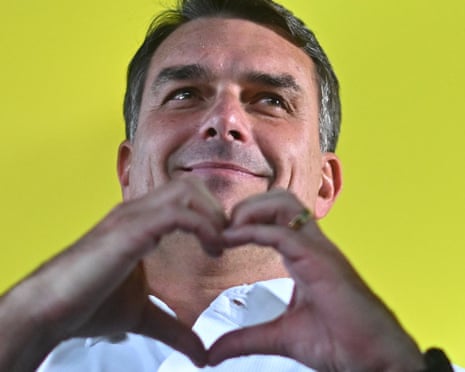 Flavio Bolsonaro smiles and looks upward while making a heart shape with his hands