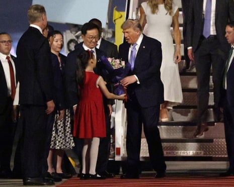 Trump receives a flower bouquet from a young girl beside Chinese vice-president Han Zheng on the red carpet