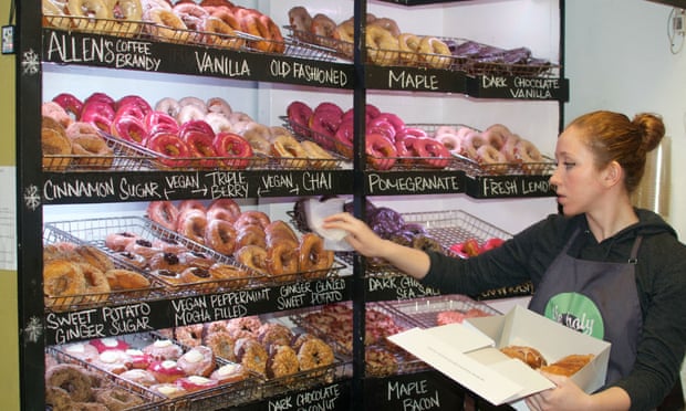 Member of staff at Holy Donut, Portland, Maine, puts doughnuts into a cardboard box from a display of the store's many doughtnuts.