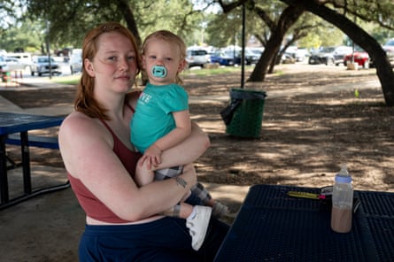 A young woman holds her young daughter in a park