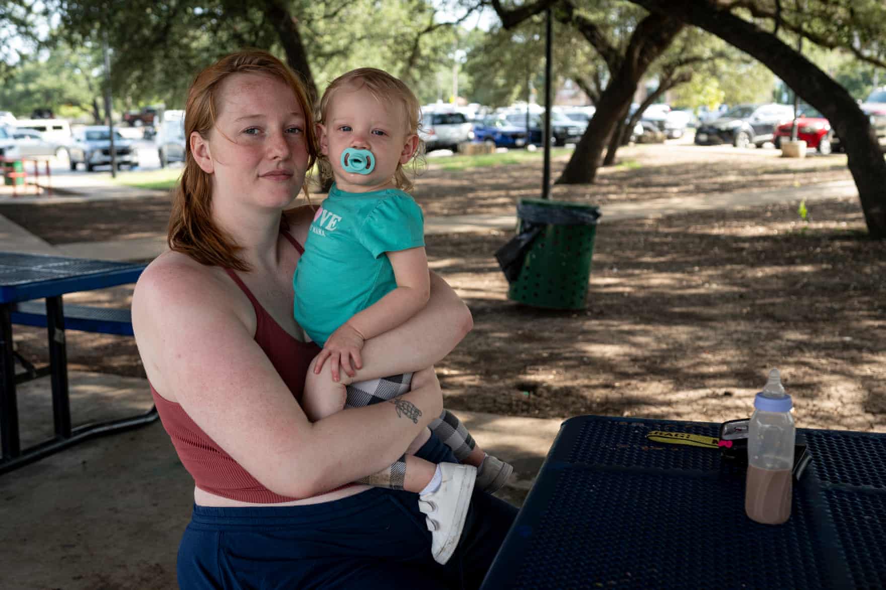 A young woman holds her young daughter in a park
