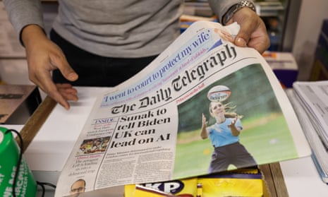 A person lifts a Daily Telegraph off a shop counter