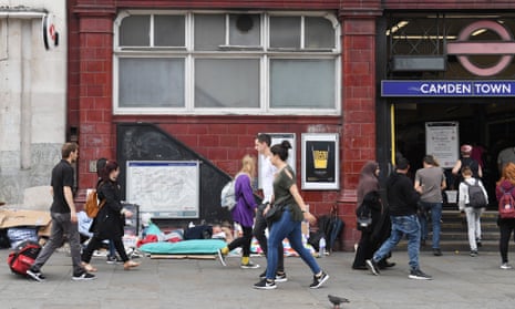 Pedestrians walk past a homeless man sleeping next to a London tube station.
