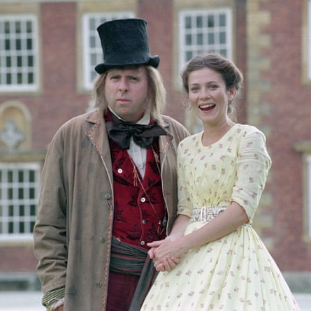Anna Friel in a yellow period dress, bareheaded, standing next to Timothy Spall in colourful Victorian clothes and a battered top hat