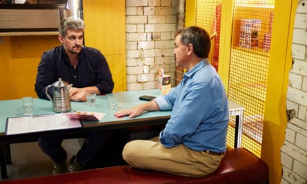 Two men, both wearing blue shirts, sitting at a restaurant table talking