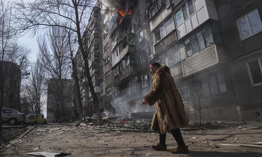 A woman walks past a burning apartment building after shelling in Mariupol, Ukraine, Sunday, March 13, 2022.