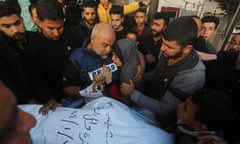 A man with the sign 'press' holds the hand of a person in a body bag.
