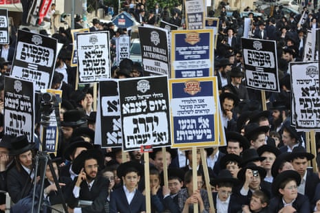 Thousands of ultra orthodox Jews demonstrate in Jerusalem against Israeli army conscription, holding placards with Hebrew writing on them.