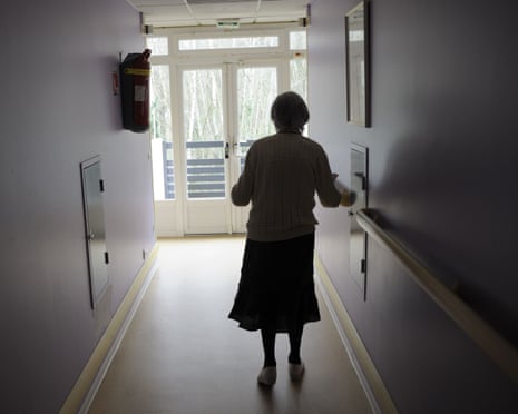 An elderly woman walks along a corridor in a care home