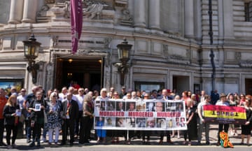 People hold banners and pictures of the victims of the infected blood scandal. One banner says 'murdered, murdered, murdered' between pictures of victims