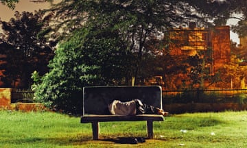 A man asleep on a park bench at night.
