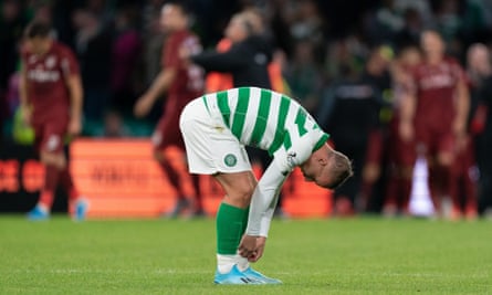 Leigh Griffiths of Celtic removes tape from his socks as CFR Cluj players celebrate in the background.