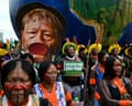 An Indigenous man holds a sign demanding respect for the Amazon next to a large cutout image of the activist Raoni Metuktire