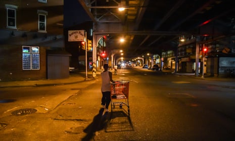 A man pulling a shopping cart on a dark street in a city