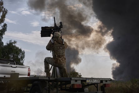 A Ukrainian soldier mans anti-aircraft weaponary amid a Russian aerial attack on Kyiv, with plumes of smoke reaching to the sky.
