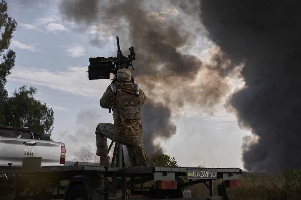 A Ukrainian soldier mans anti-aircraft weaponry amid a Russian aerial attack on Kyiv, with plumes of smoke rising into the sky