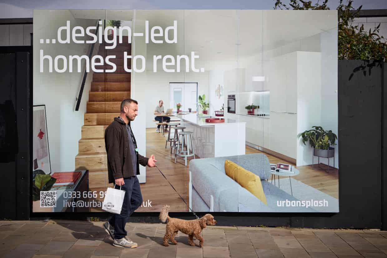 A man walks a curly haired dog past a New Islington billboard advertising homes to rent