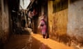 A woman stands ankle deep in murky water in a slum alleyway.