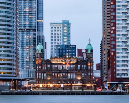 An old red brick building with towers in between modern skyscrapers on the waterfront