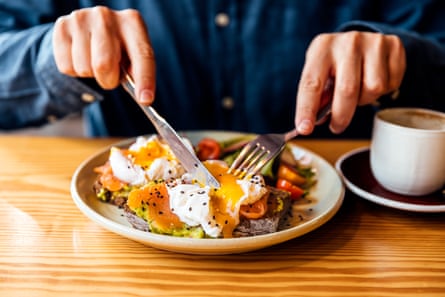 Man eating healthy breakfast of avocado toast with salmon and poached egg.