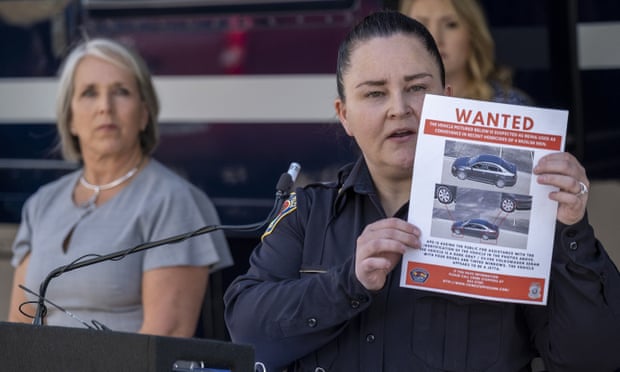 A woman stands in front of a podium with a microphone holding up a flyer with the word 'Wanted' across the top.