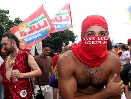 Bare-chested man at rally with red scarf round lower half of face with pro-Lula slogan.