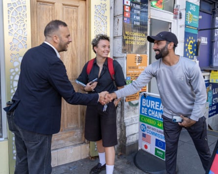 Polanski shakes hands with a man outside a shop, as a smiling party activist looks on
