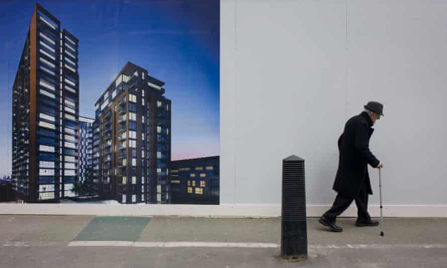 An elderly man walks bent past a regeneration project hoarding image at Elephant &amp; Castle, London.