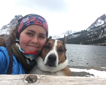 A woman and her dog next to a body of water and snow-covered mountains