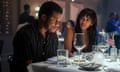 Black man sitting at table looks down as Black woman looks at him