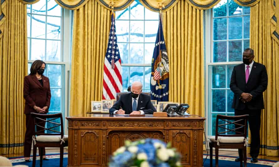 Flanked by Vice President Kamala Harris and Secretary of Defense Lloyd Austin, President Joe Biden signs an executive order in the Oval Office of the White House repealing the ban on transgender people serving openly in the military.