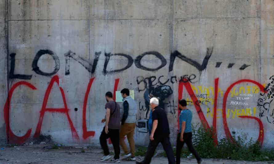 Men walk past graffiti in the make-shift immigrant camp, known as the jungle, in Calais.