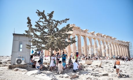 The Acropolis under a blue sky, with people sheltering in the shade of a tree