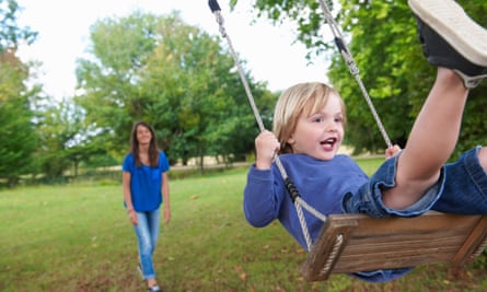 Small boy playing on swing in park as young woman stands behind