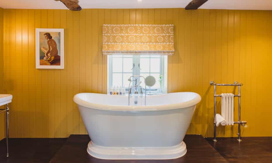 A yolk-yellow bathroom with a white rolltop bathtub in the middle of the room