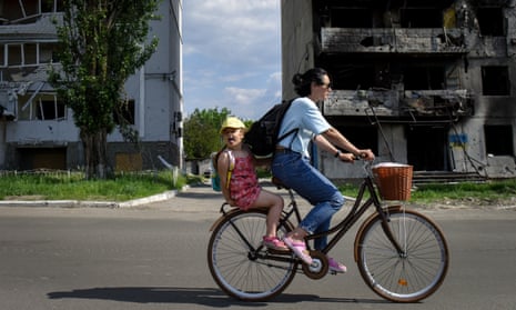 Woman and child riding on bicycle past burnt-out flats in outer Kyiv.