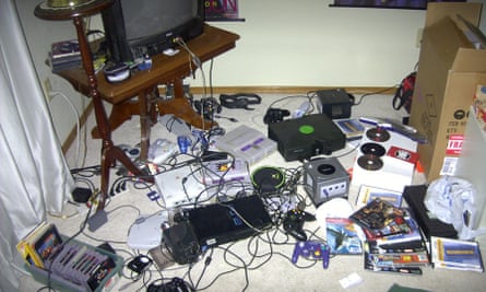 A room with bits of computers, games consoles, cables, magazines and CDs all over the floor