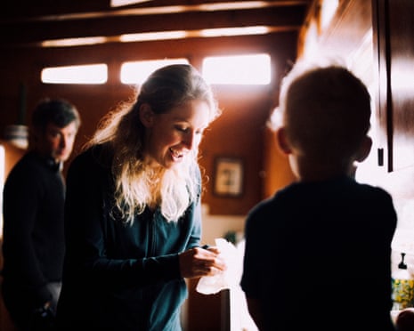 In a still from You Can See Everything, Elizabeth Holmes talks to one of her children, while Nathan Fielder is seen in the background