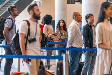 People Lined Up At A Check-In Area At The AirportDiverse people checking in at the airport. Lining up, holding luggage and boarding passes.