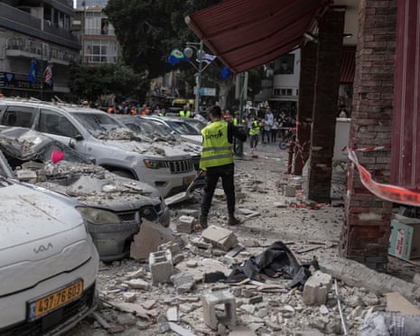 मध्य इज़राइल के रामत गान में ईरानी प्रक्षेप्य हमले से प्रभावित एक इमारत की सड़क की सफ़ाई करते नगरपालिका कर्मचारी