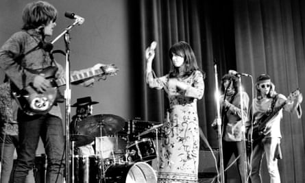 A young female singer performs passionately with her hand raised on stage alongside three male musicians playing guitar and drums, capturing the vibrant energy of youth culture and music.