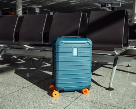 A teal-colored suitcase on ground next to a row of seats