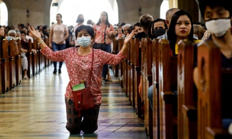 A Filipino Catholic wearing a protective mask amid a coronavirus scare kneels to pray