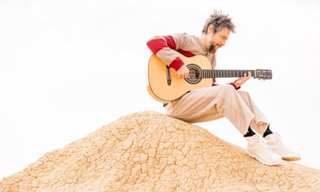 Raül Refree sitting playing his guitar on what looks like a hill of baked earth in a studio
