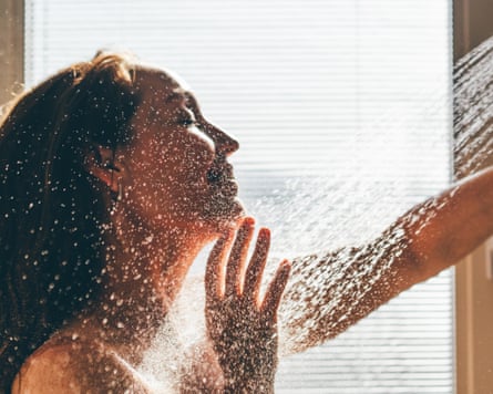 Head and shoulders image of a woman taking a shower in a well-lit, bright shower room.