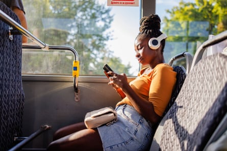 Woman on bus wearing headphones while listening to music on her phone