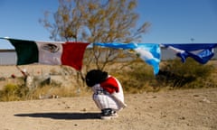 Small girl shelters from cold wind in front of Mexican and other flags at US-Mexico border