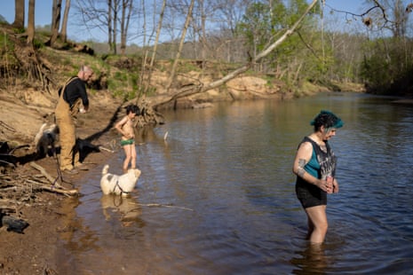 A man, child, woman, and dog walk in a creek