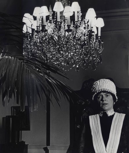 Black and white photograph of a parlourmaid standing beneath a chandelier