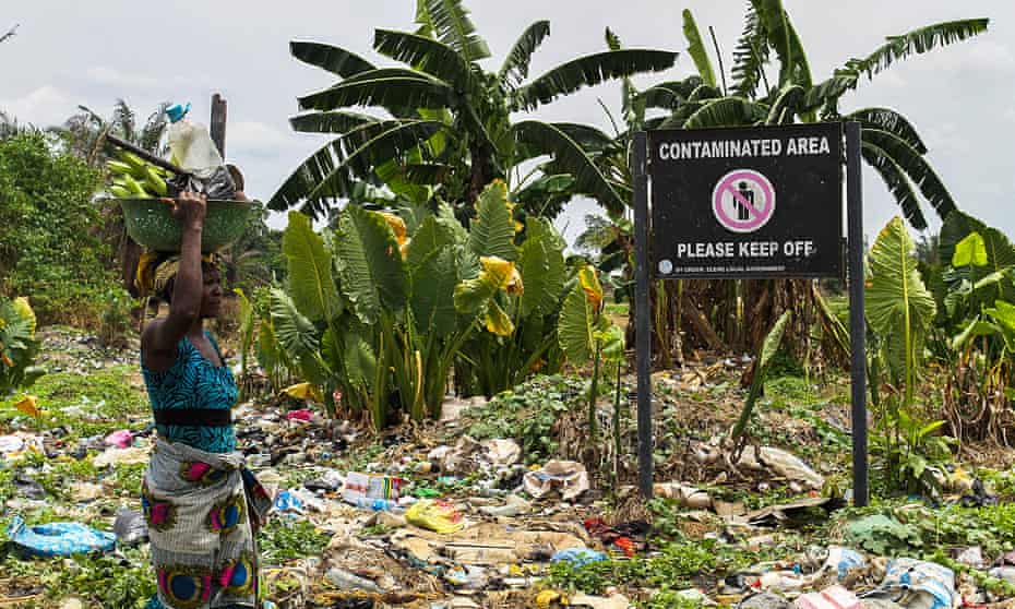 A woman walks past a sign on polluted land in the Ogale community warning of contamination in 2016
